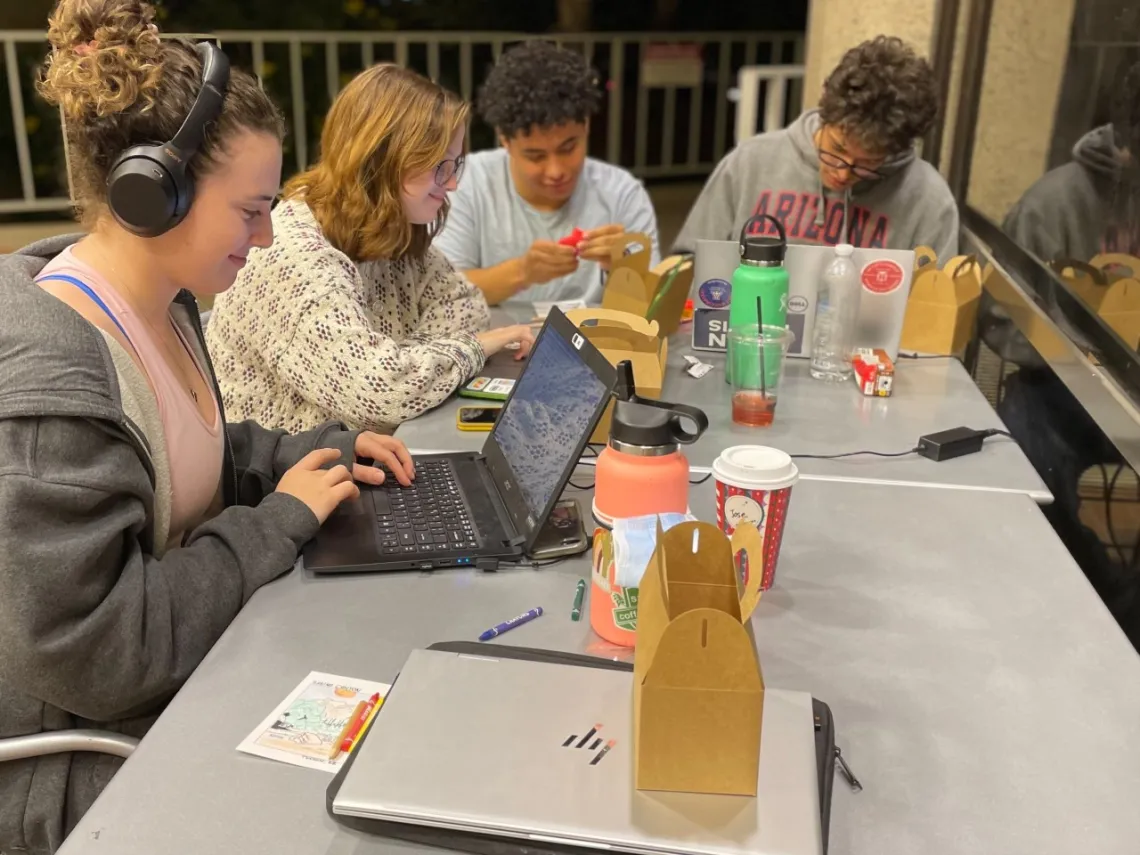 four students sitting at a table looking at self-care kits and working on laptops