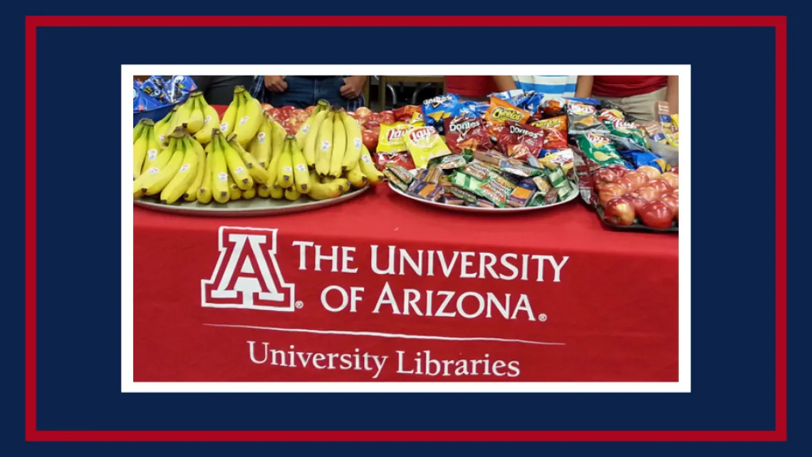 bananas, apples, chips, cookies and snacks on a red UA Libraries tablecloth